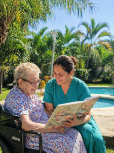 Elderly woman in wheelchair enjoying outdoor garden time with caregiver at Villa Alegría Nursing Home in Costa Rica