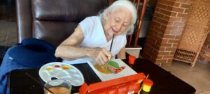 Elderly woman painting with bright colors during an art activity at Villa Alegría.