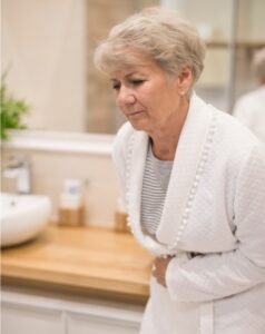 Image of an older adult woman clutching her abdomen with a pained expression due to constipation