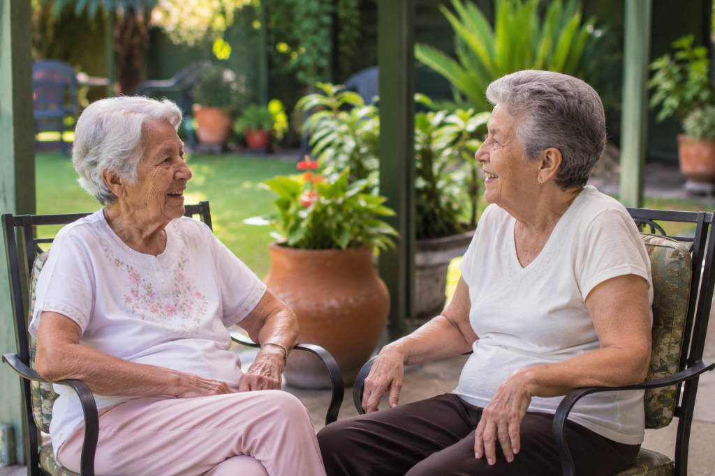 Two older adults enjoying a friendly conversation in the garden of an assisted living community.