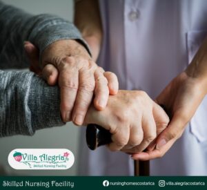 representative image of a nurse affectionately holding the hands of an elderly person with her cane, which represents Villa Alegría in the care, love and support that we provide to our residents