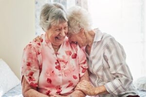 Two elderly women laughing and hugging, sharing a joyful moment together