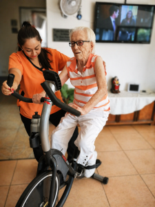 Elderly woman exercising on a stationary bike with caregiver assistance at a nursing home in Costa Rica
